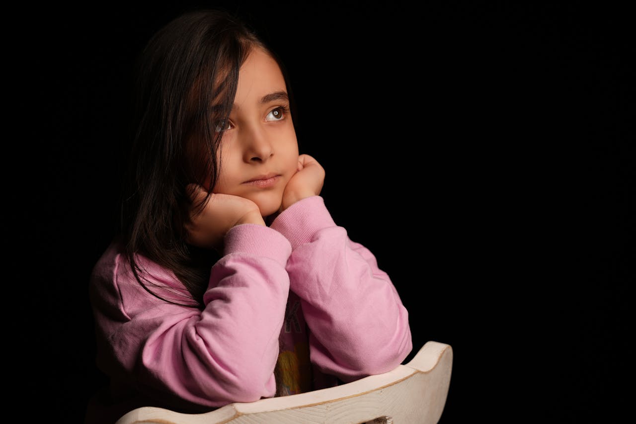 Portrait of a girl in a pink sweater looking thoughtfully upwards in a dark setting.
